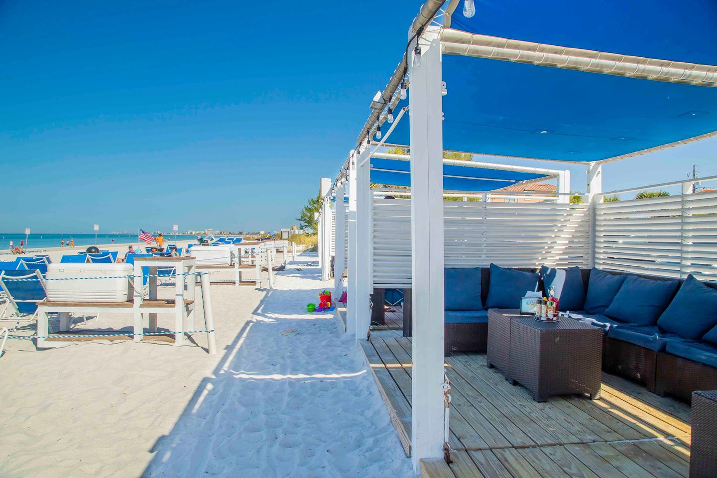 Caddy's Treasure Island-min Beachfront seating area at Caddy's Treasure Island with blue cushions, sandy path, and scenic ocean view, highlighting a vibrant atmosphere for relaxation and dining.