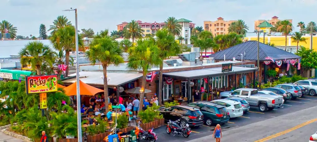 Ricky T's - Treasure Island-min Ricky T's bustling eatery in Treasure Island, featuring outdoor seating, palm trees, and a lively atmosphere, ideal for enjoying local cuisine after a golf cart rental.